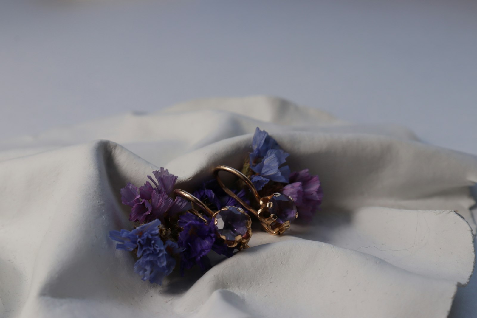 Gold earrings rest on purple flowers and fabric.