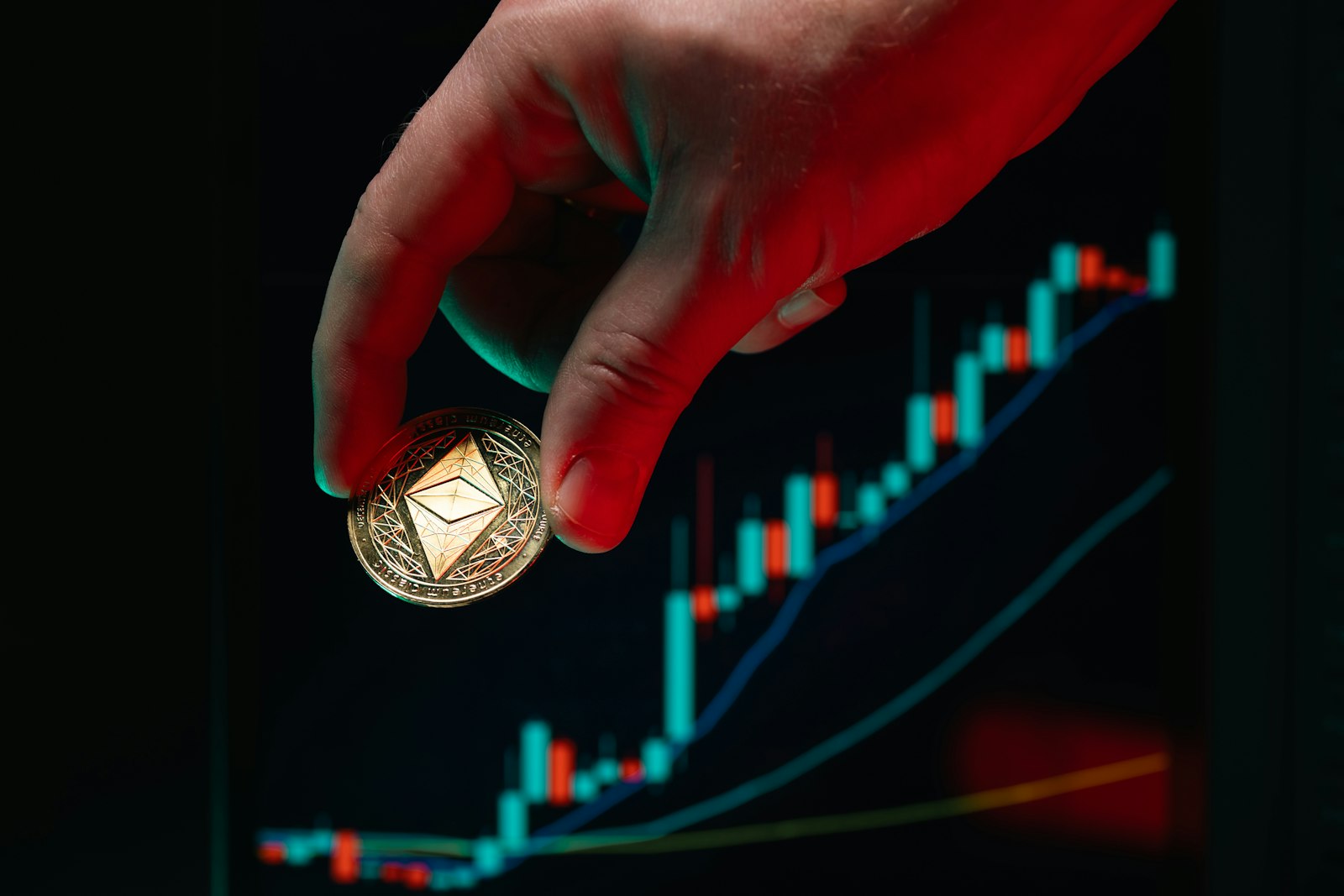 Hand holds ethereum coin over the stock chart.