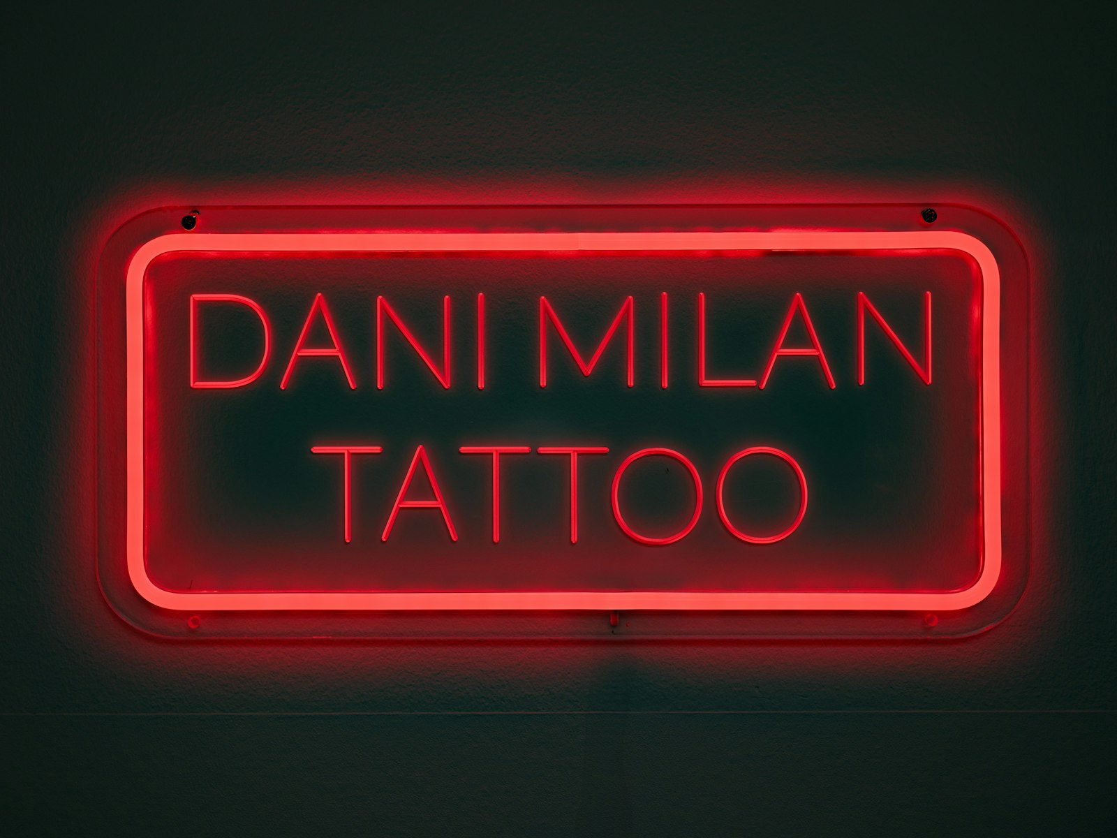 A red neon sign that says dani milan tattoo